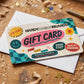 A decorative gift card for Handy Dandy Brandy rests on top of a white envelope on a rustic wooden surface scattered with star-shaped confetti.
