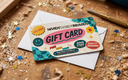 A decorative gift card for Handy Dandy Brandy rests on top of a white envelope on a rustic wooden surface scattered with star-shaped confetti.