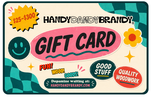 HandyDandyBrandy gift card design with a cream background, teal checkered corner accents, a yellow starburst reading '$25-$300', and large pink 'GIFT CARD' text. Decorative stickers include a smiley face, flower, stars, and phrases like 'FUN! WOOD! GOODS!' and 'Dopamine waiting at: HANDYDANDYBRANDY.